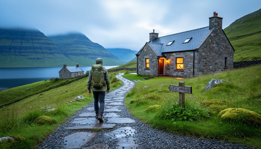 A hiker with a daypack walks along a Scottish Highlands trail toward a stone guesthouse with mountains and a loch in the distance.